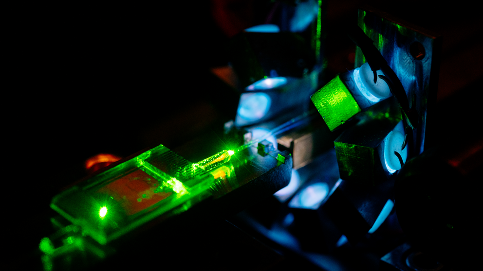Aufnahme von einem Laser, dessen grnes Licht auf einen durchsichtigen Chip scheint. Dunkler Hintergrund