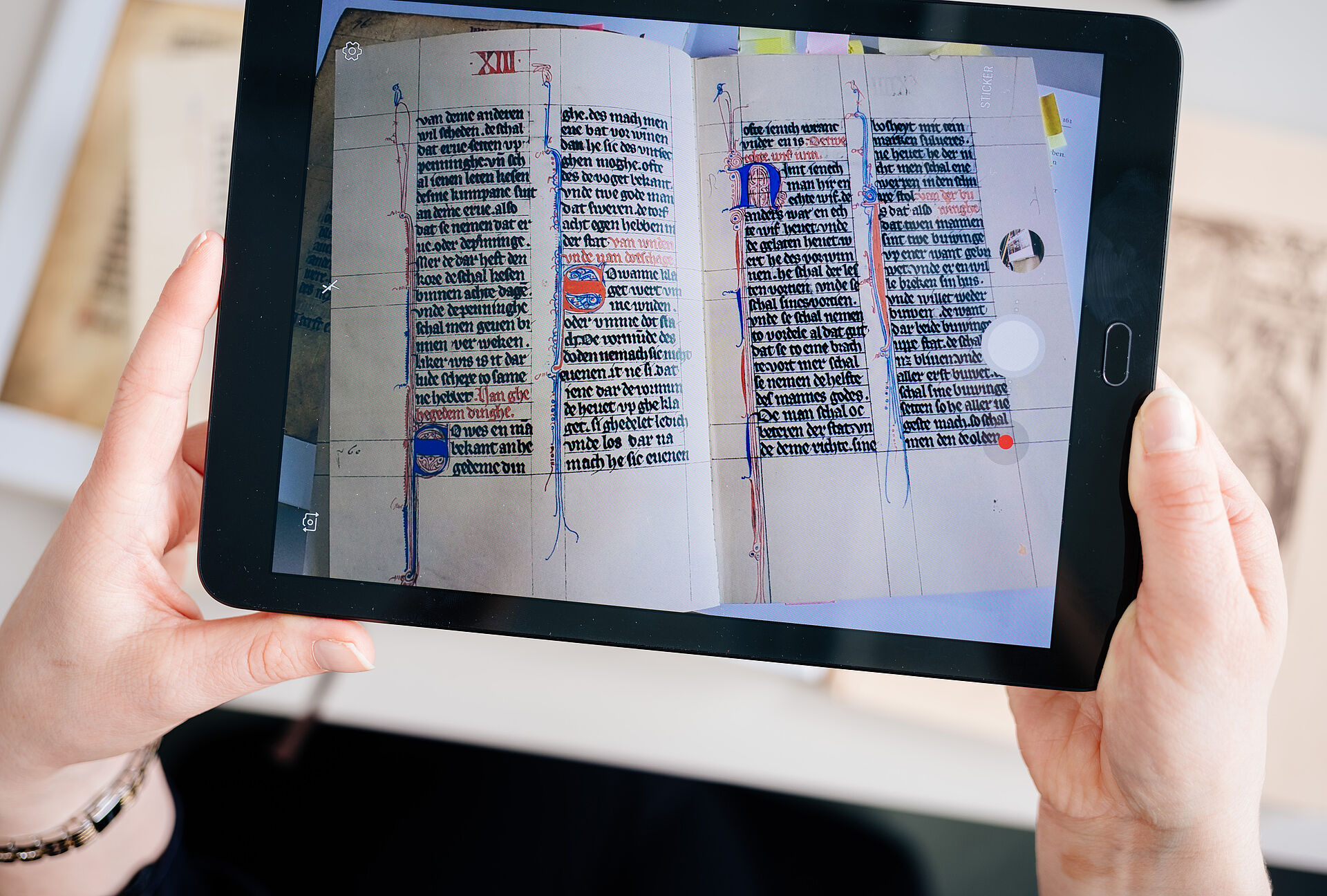 Auf einem beidh?ndig gehaltenen Tablet wird ein Buch mit mittelalterliche Schrift angezeigt